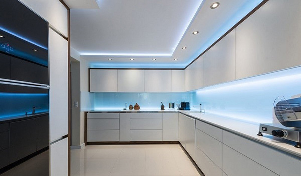 نمایی از طراحی نورپردازی لایه‌ای در آشپزخانه مدرن، با استفاده از لاین نوری توکار LED در سقف به عنوان نور محیطی، و نصب چراغ خطی آویز برای تأمین نور وظیفه‌ای متمرکز و دکوراتیو بر روی جزیره مرکزی.